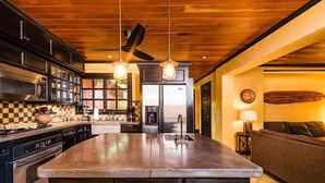 Une cuisine moderne dotée d’un îlot central, d’appareils électroménagers en acier inoxydable et de luminaires suspendus.