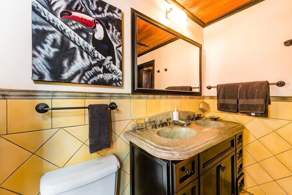 Ein Badezimmer mit einem Doppelwaschbecken, einer Toilette, einem Handtuchhalter und einem großen Spiegel.