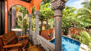 Un espace extérieur avec une piscine, agrémenté de colonnes décoratives, d’un banc en bois et d’une végétation luxuriante.