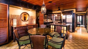 Un vaste espace dédié à la salle à manger, avec une table ronde et des chaises, une cuisine en arrière-plan et des panneaux de plafond en bois.