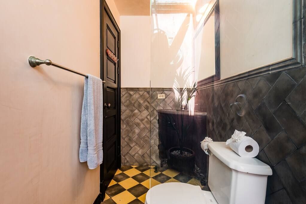A bathroom with a checkered floor, a towel hanging on a metal rod, a toilet, and a trash bin.