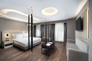 A modern hotel room with a large bed, bedside table, and a flat-screen TV mounted on the wall.