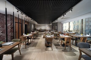 A spacious dining area with multiple tables and chairs, a marble wall, and a ceiling with a grid pattern.