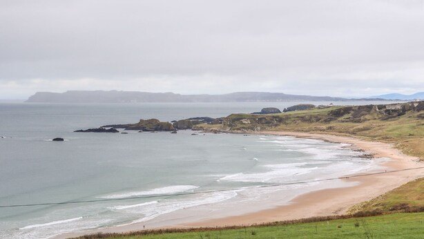 A coastal landscape with a sandy beach, rocky outcrops, and grassy hills. - 4 The Cloisters (Bushmills)
