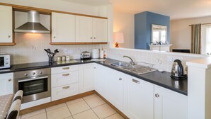A modern kitchen with white cabinets, a stainless steel range hood, a built-in oven, a microwave, and a sink with a dish rack. - 4 The Cloisters (Bushmills)