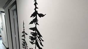 Un couloir dont un mur est décoré de silhouettes noires représentant trois espèces d’arbres différentes.