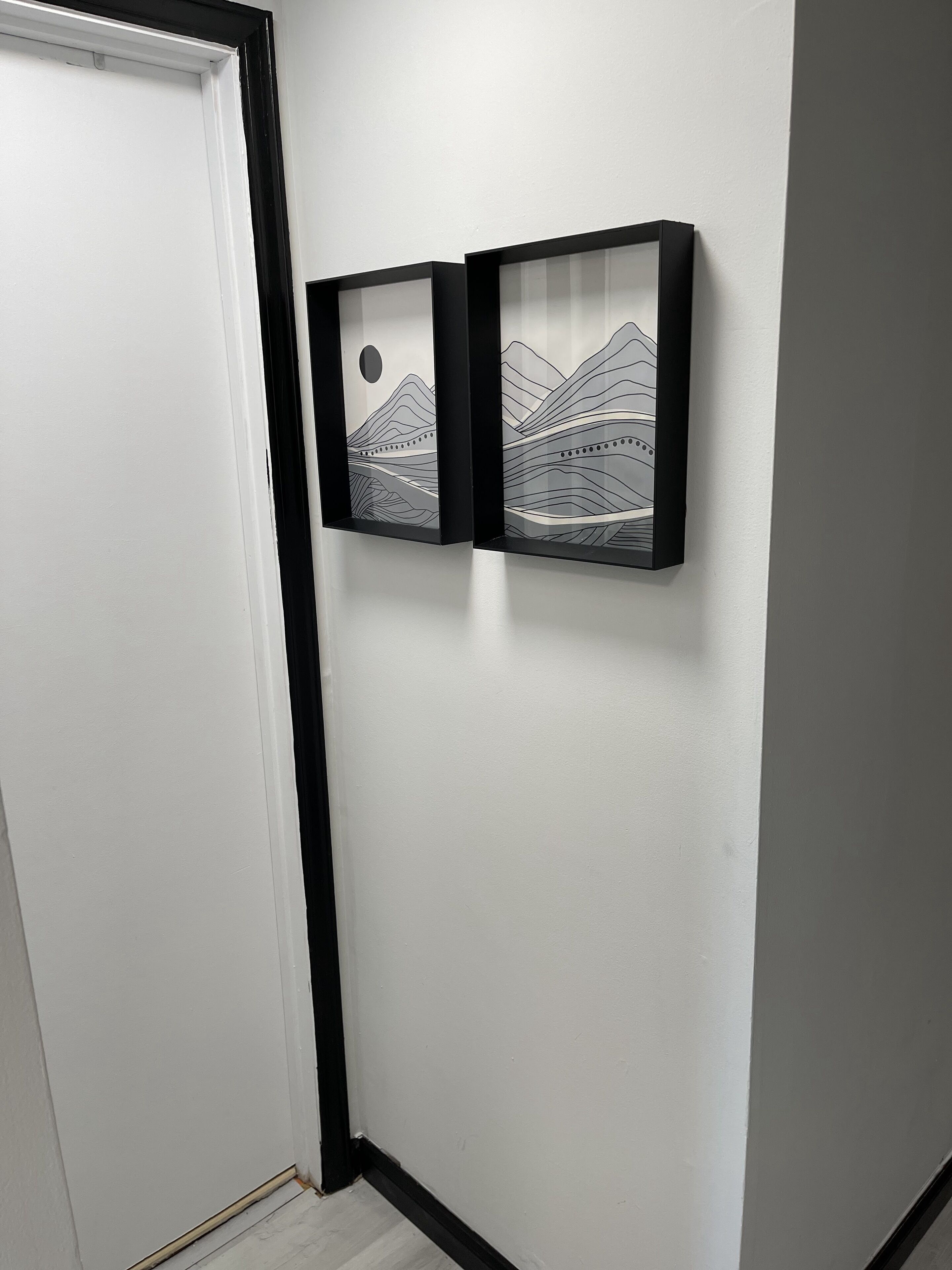 Un couloir avec deux œuvres d’art encadrées accrochées au mur, une porte et un sol blanc.