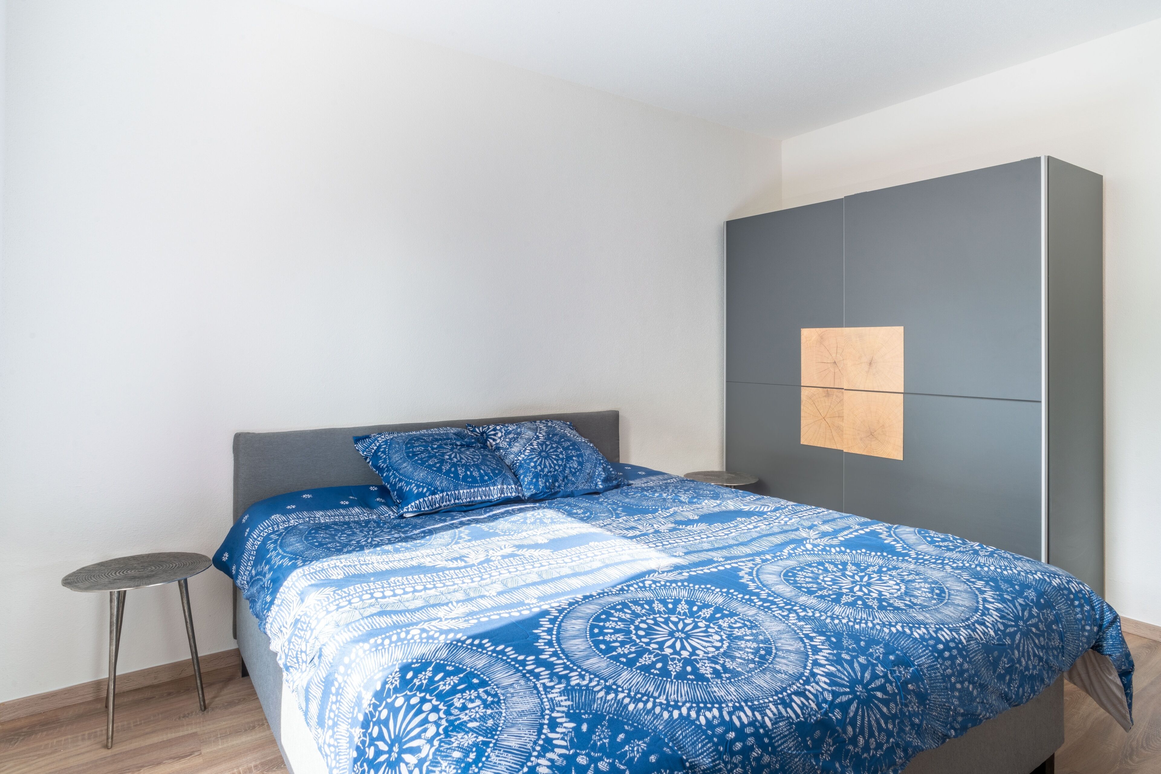 Ein Schlafzimmer mit einem Bett, einem grauen Kleiderschrank und einem kleinen Hocker.