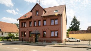 A two-story building with a red-tiled roof, a small entrance canopy, and a car parked in the driveway.