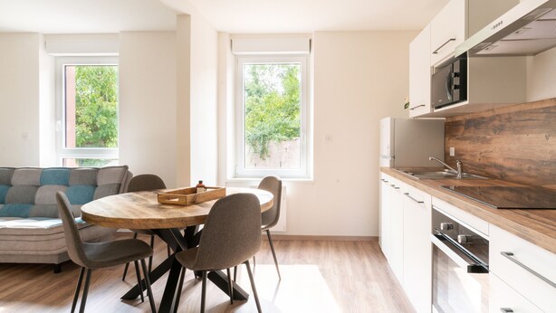 Une cuisine moderne avec des plans de travail en bois, un four encastré et un coin repas comprenant une table ronde et des chaises.