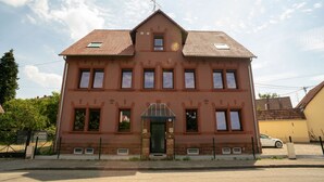 Un bâtiment à deux étages doté d’une façade symétrique, d’une entrée centrale surmontée d’un petit auvent et d’un toit recouvert de tuiles.