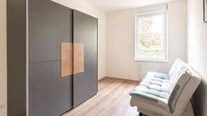 Une chambre moderne dotée d’une grande armoire, d’un banc rembourré et d’une fenêtre donnant sur un paysage verdoyant.