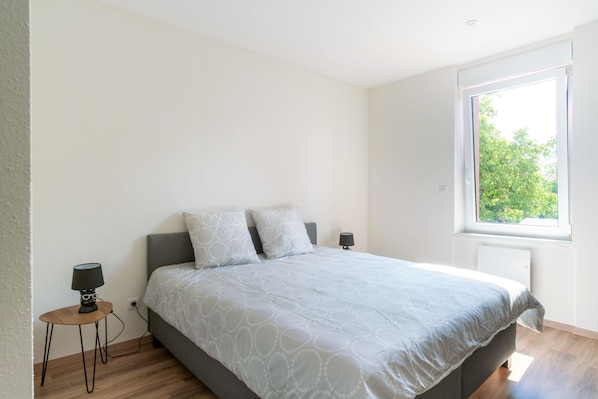 A bedroom with a bed, two bedside lamps, a window, and a small table.