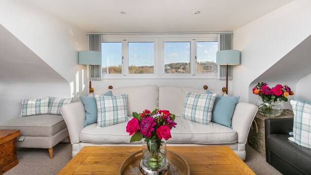 En moderne stue med en hvid sofa, blå og hvide puder, et træbord og en vase med blomster.