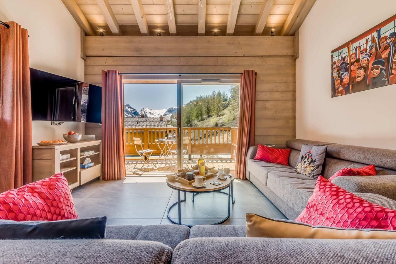 Un salon moderne avec un canapé, une table basse et un téléviseur. Il y a un balcon avec vue sur les montagnes.