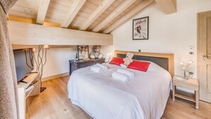 A bedroom with a large bed, wooden beams, a framed picture on the wall, and a bedside table with a lamp.