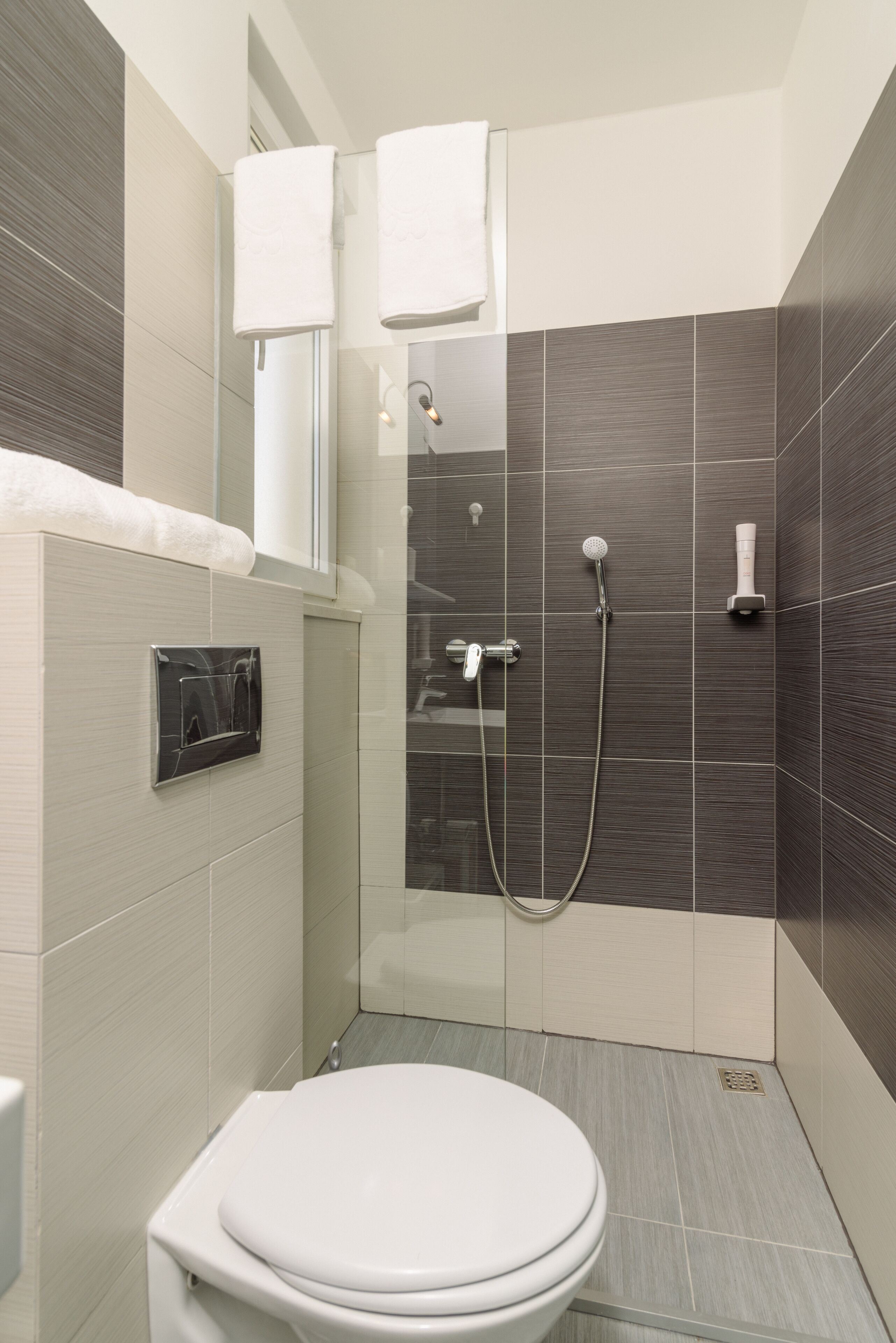 Ein modernes Badezimmer mit Toilette, einer Dusche inklusive Handbrause und einem Handtuchhalter.