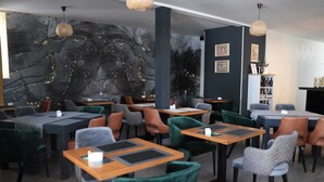 Een restaurant met tafels, stoelen, een muurschildering en hangende lampen.