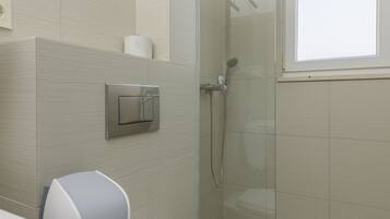 A modern bathroom with a toilet, a hand dryer, a towel rack, and a glass shower enclosure.