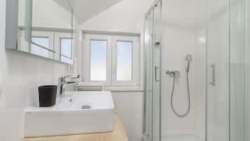 A modern bathroom with a white sink, a black cup, a glass shower enclosure, and a window providing natural light.