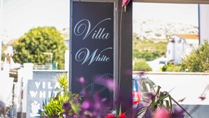 Naamplaatje voor Villa White met een helder uitzicht op de omgeving, inclusief geparkeerde auto's en groen.