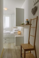 Ein kleines, gut beleuchtetes Schlafzimmer mit Bett, Nachttisch und Holzstuhl.