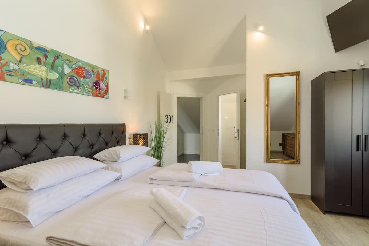 Una habitación de hotel con una cama grande, un cabecero, un cuadro, un espejo y un armario.
