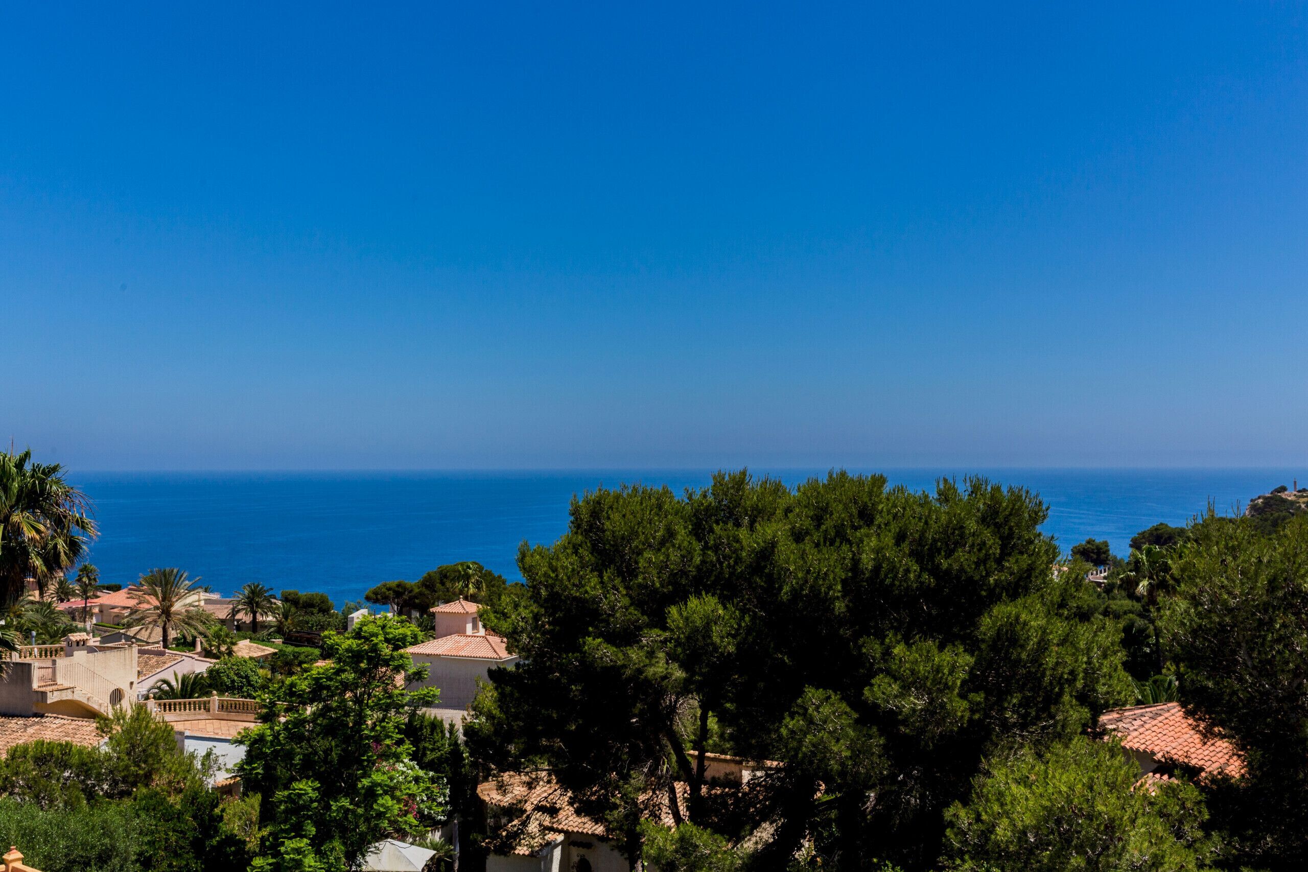 A coastal town with Mediterranean architecture, clear blue sky, and the sea in the background.