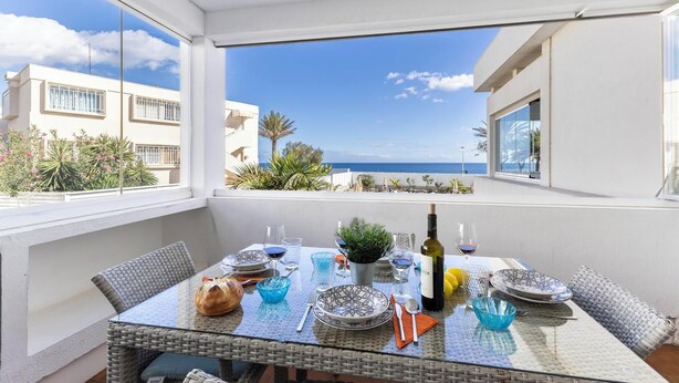 A balcony with a table set for dining, overlooking a coastal view.