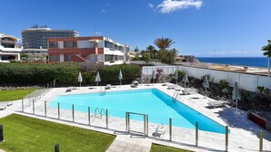 A swimming pool with a clear view of the ocean, surrounded by a fenced area with lounge chairs and umbrellas.