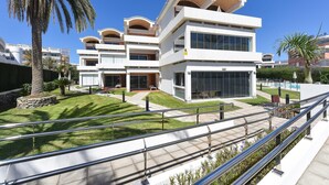 A modern multi-story building with balconies, large windows, and a well-maintained lawn.