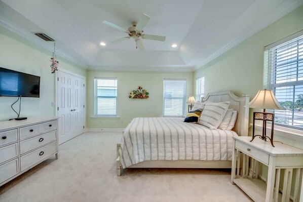 A bedroom with a bed, a nightstand, a TV, a ceiling fan, and a window. - 260 Key West Luxe Beachfront Home with Shared Pool (Fort Myers Beach)