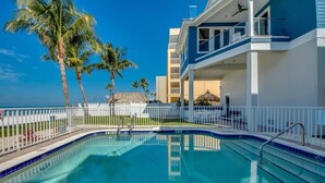 A swimming pool with a white fence, palm trees, and a building with balconies.