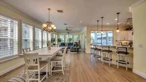 A spacious kitchen with a dining area, large windows, and a central chandelier.