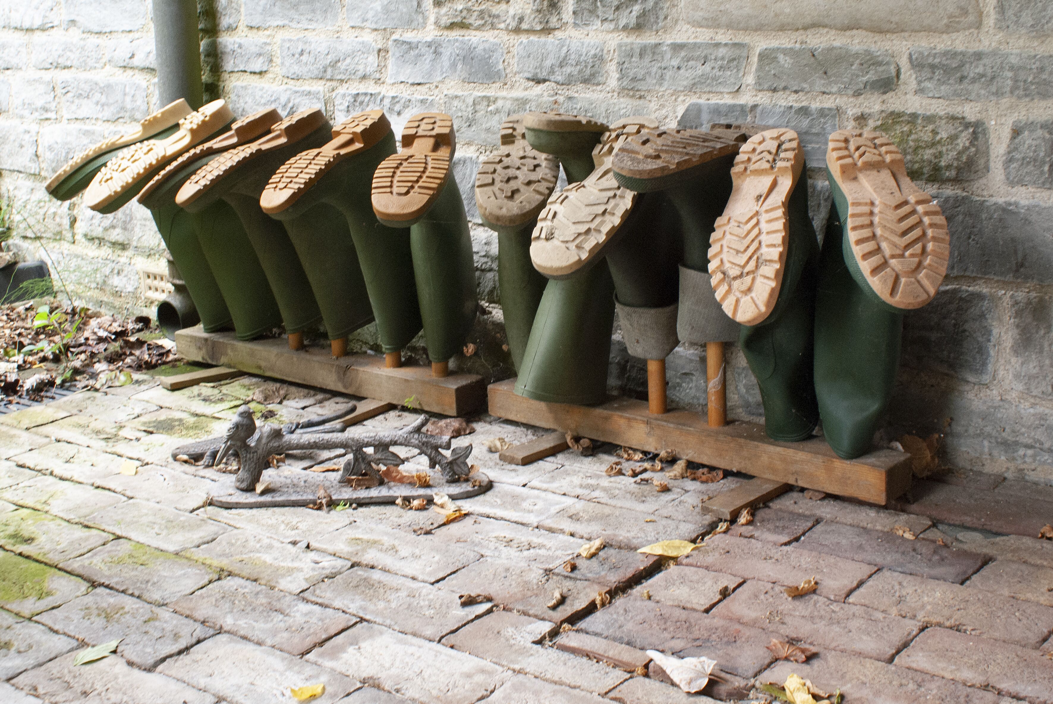 Une rangée de bottes vertes, aux semelles présentant différents motifs, est exposée contre un mur de pierre.