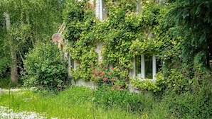 A stone house with ivy-covered walls, a brick pathway, and a garden with various plants and flowers.