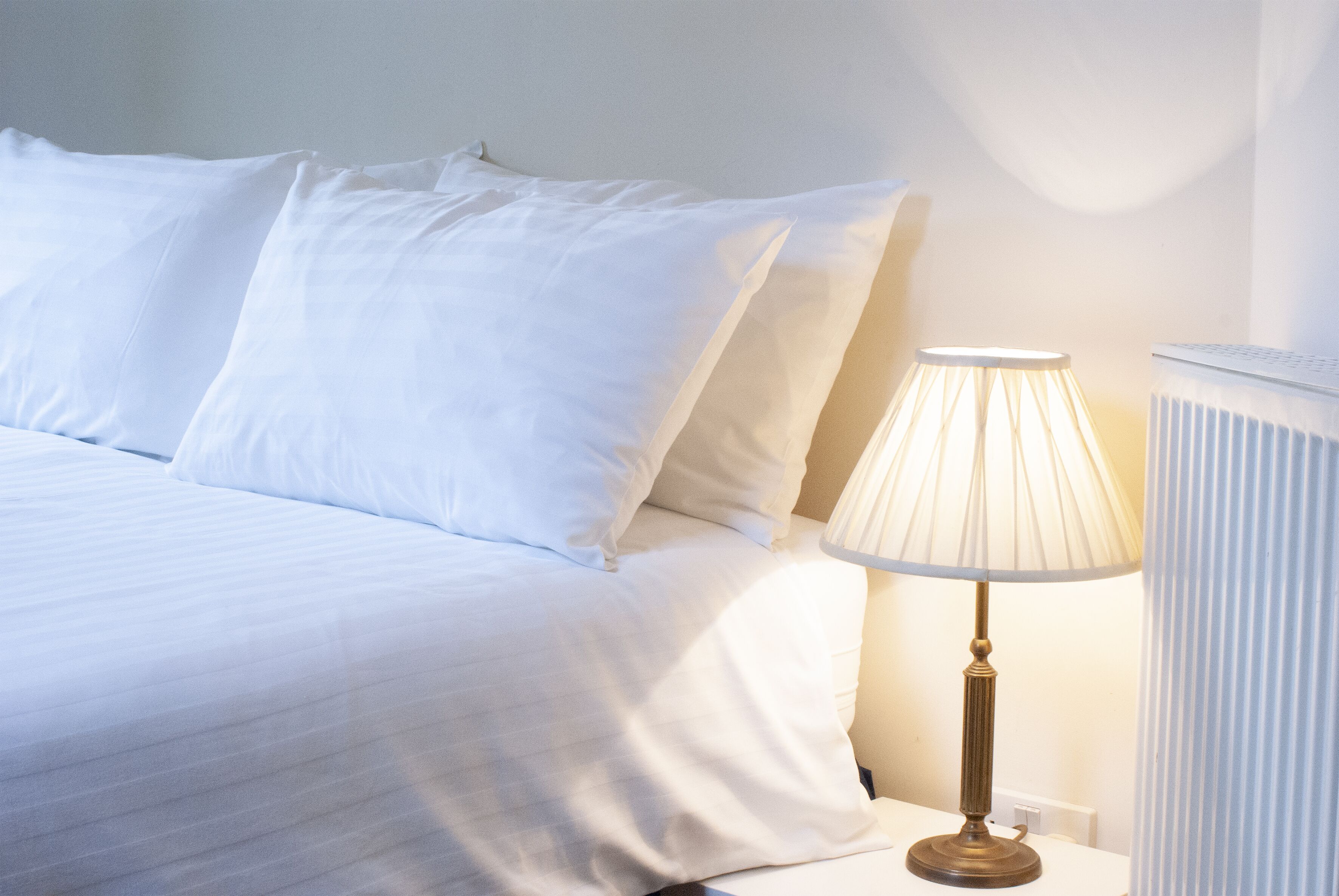 Un lit bien fait, avec du linge de lit blanc et une lampe de chevet.