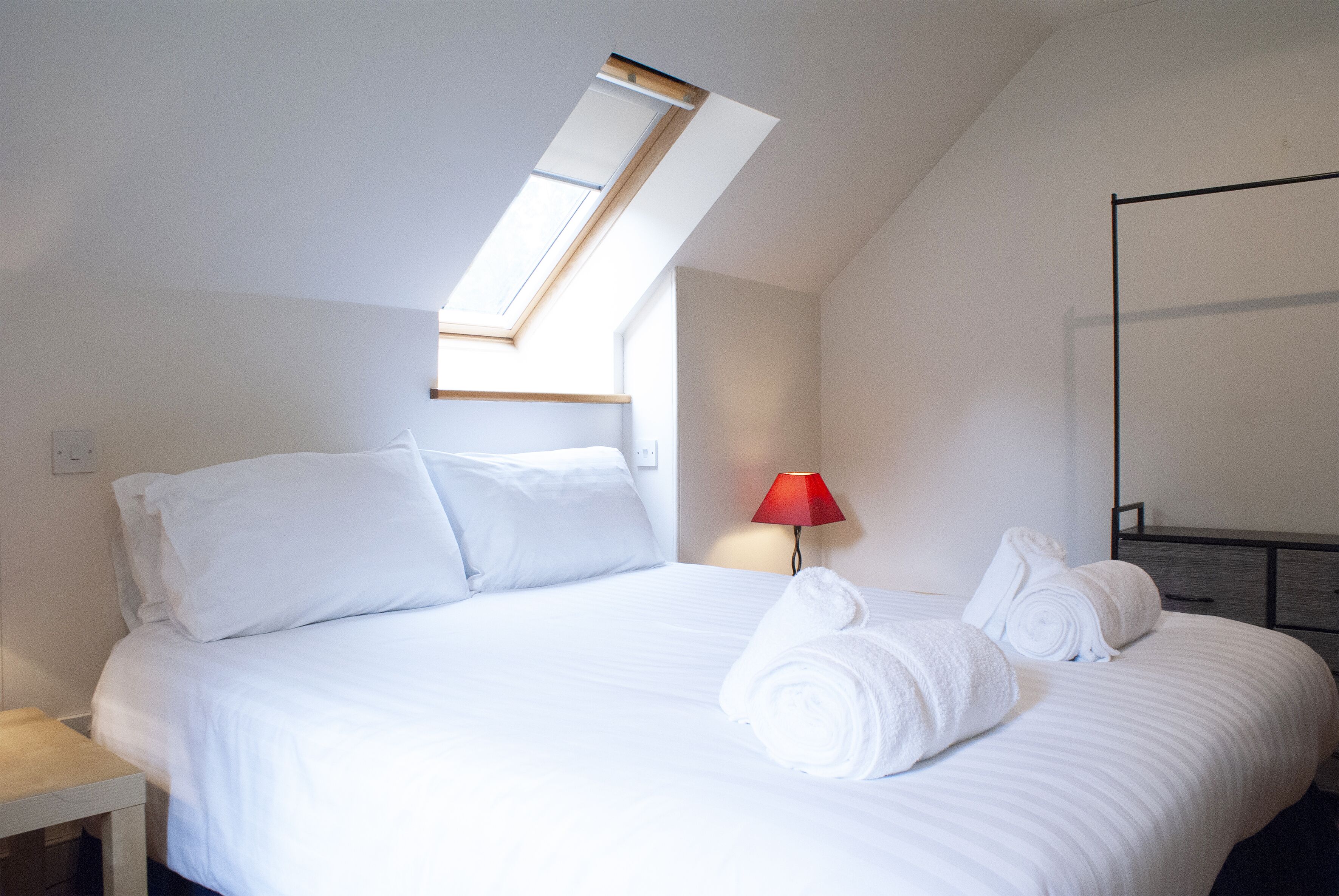 A hotel room with a bed, a nightstand, a lamp, and a skylight.