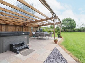 Un patio cubierto con un jacuzzi, mobiliario exterior y un sendero de piedra que conduce a una zona verde.