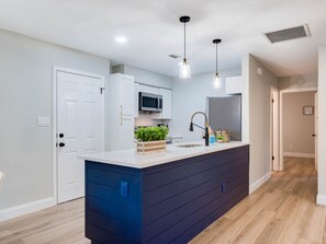 A modern kitchen with a central island, white cabinets, a microwave, and pendant lighting.