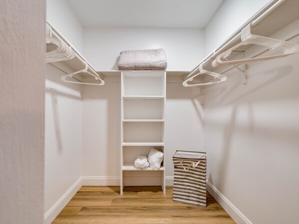 A walk-in closet with white shelving, a hanging rod, and a striped laundry basket.