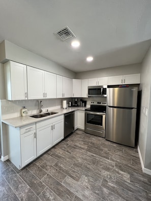 A modern kitchen with white cabinets, stainless steel appliances, and a herringbone-patterned floor.