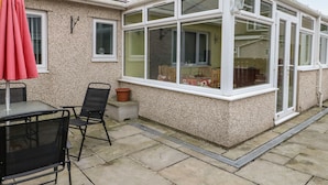 A conservatory with a glass roof, a patio table, and chairs. - 11 Bro Celyn (Holyhead)