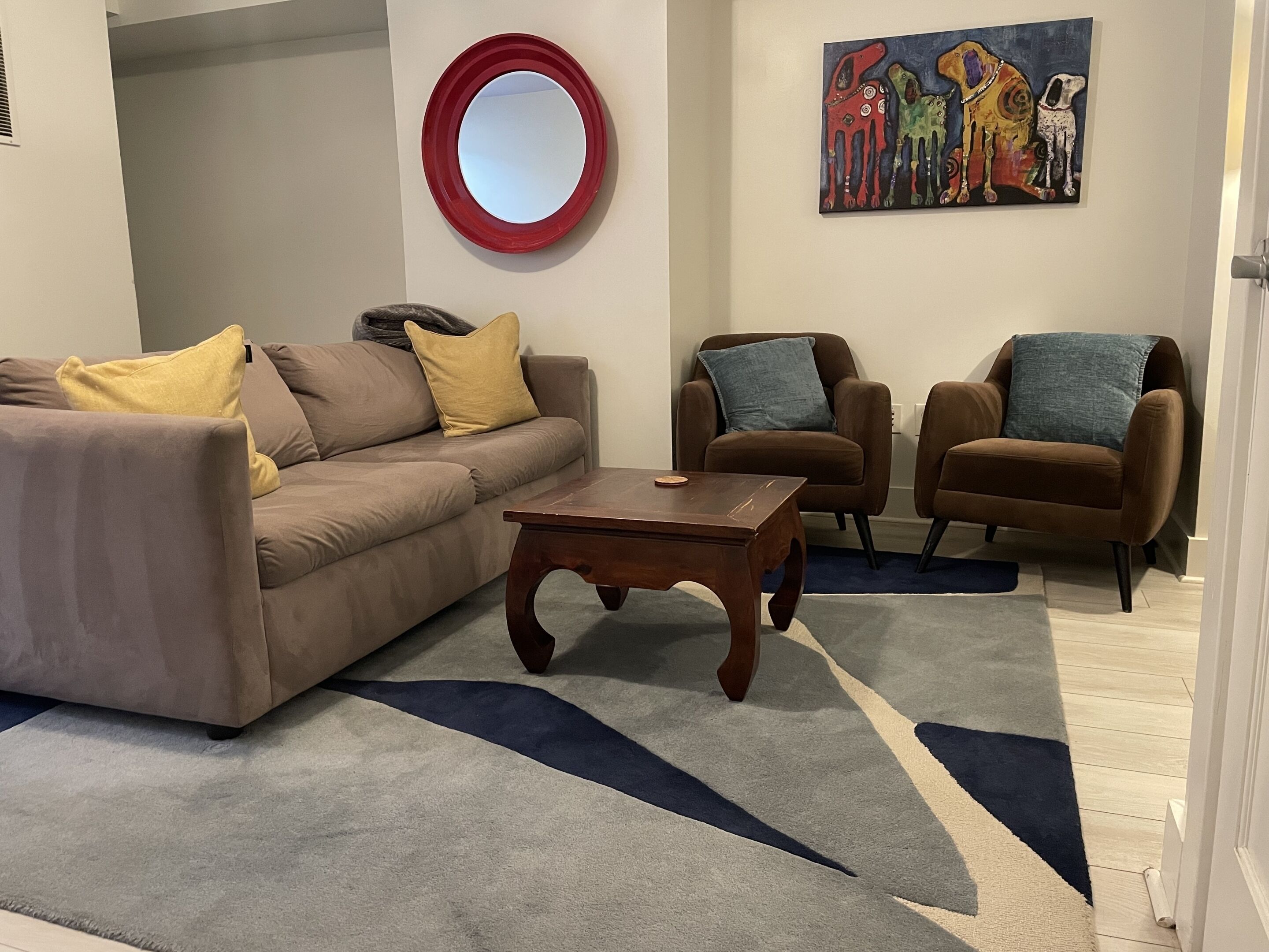 A living room with a sofa, two armchairs, a coffee table, a round mirror, and a painting on the wall.