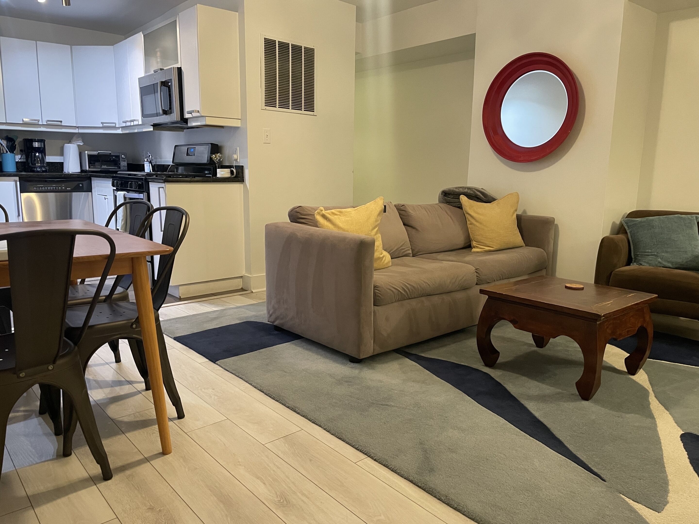 A modern living room with a sofa, coffee table, and dining area with chairs and a kitchen in the background.