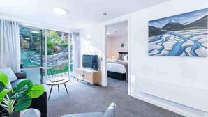 Een moderne hotelkamer met een groot raam, een schilderij van een rivierlandschap, een bed, een bureau en een televisie.