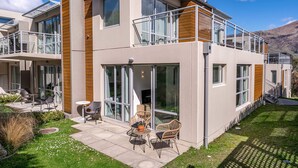 Een modern huis met twee verdiepingen, grote glasramen, een balkon en een patio met buitenmeubilair.