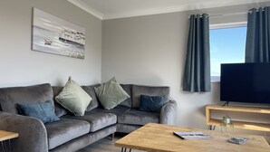 En moderne stue med en grå sofa, et træbord og et fladskærms-tv.