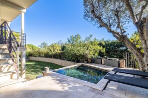 A swimming pool with a stone deck, a staircase, and a view of the surrounding garden and trees.