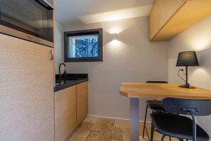 A compact kitchen with a built-in oven, a window with a view, a small dining table, and a chair.